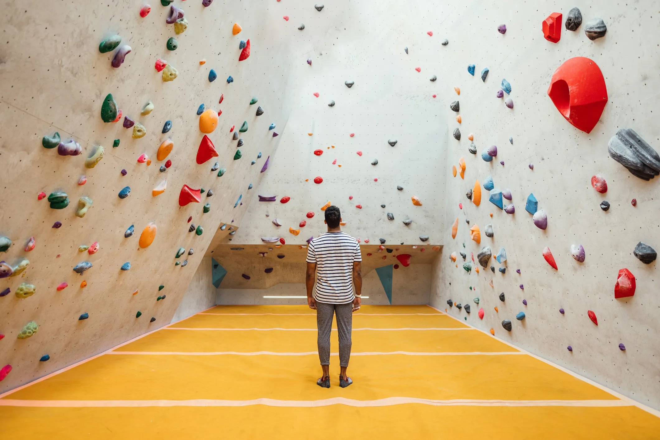 A wide angle rear view of a man looking at the expansive climbing wall at an indoor climbing center