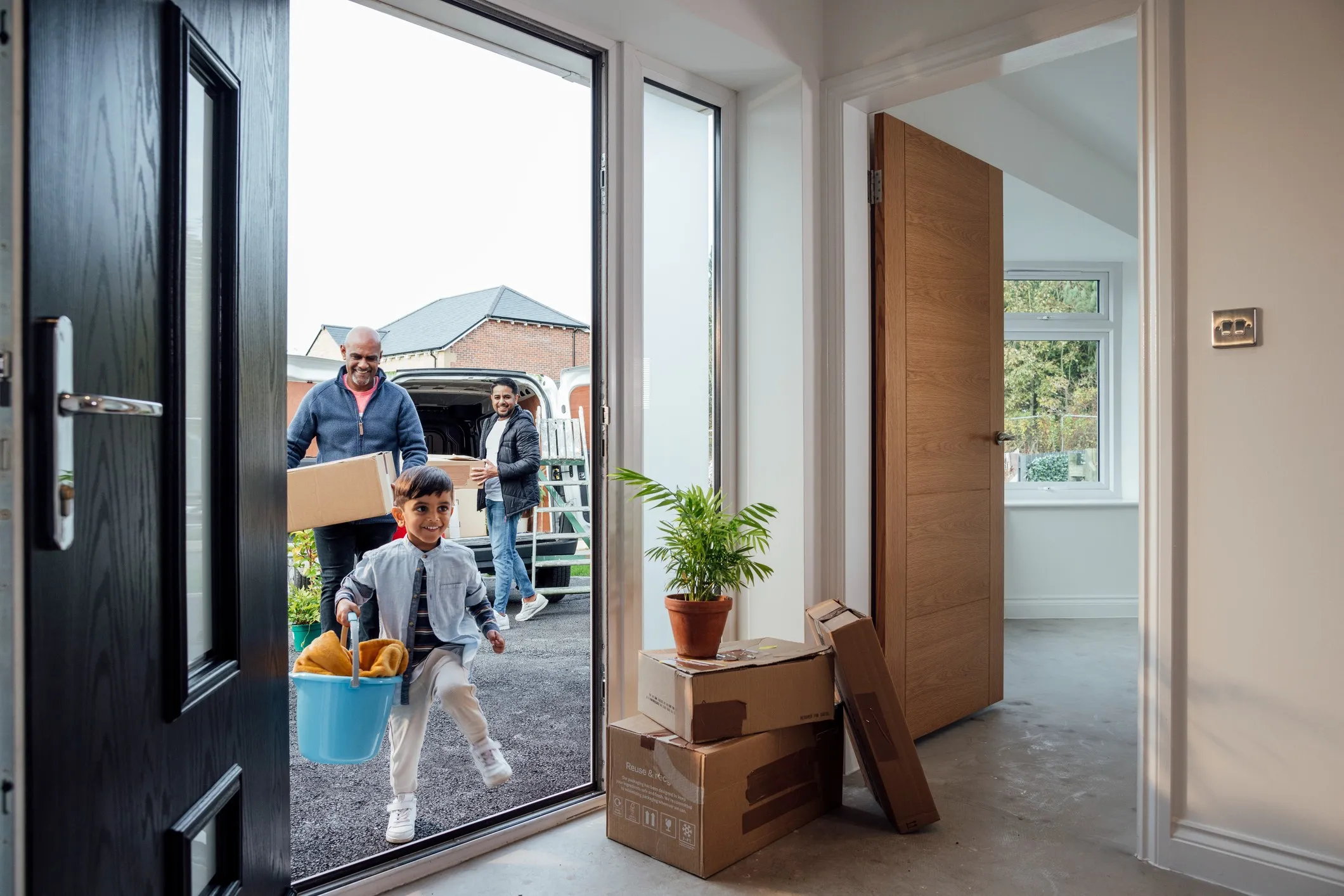 A shot of a grandfather with his son and grandson wearing casual clothing, unloading boxes and furniture from the rear of a moving van